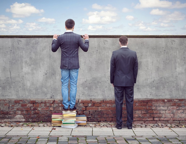 Zwei Männer an der Wand. Einer schaut dagegen, der anderer steht auf Büchern und schaut drüber